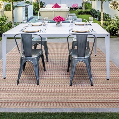Mesa de jantar branca com quatro cadeiras metálicas cinzentas e tapete geométrico num jardim