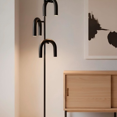 Abajur de pé preto com três braços curvos ao lado de móvel de madeira clara