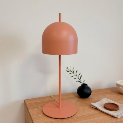 Candeeiro de mesa terracota com base redonda sobre cómoda de madeira com vaso negro e ramo verde