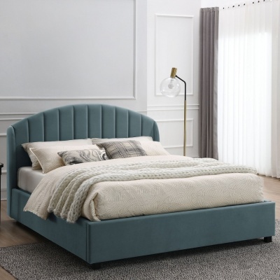 Cama estofada azul com roupa de cama bege e manta branca, almofadas e luminária dourada ao lado