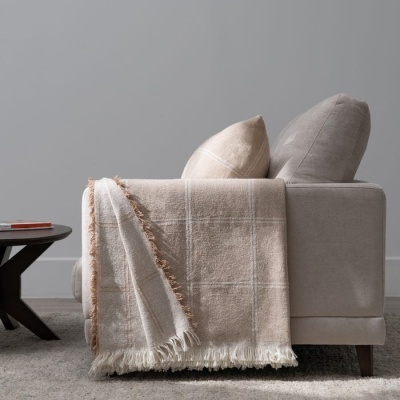 Sofá cinzento com almofadas e manta bege xadrez ao lado de mesa baixa preta