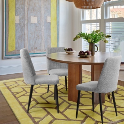 Mesa redonda de madeira com três cadeiras cinza sobre tapete amarelo geométrico, jarro com planta e taças com frutas