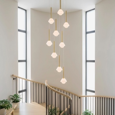 Lustre pendurado com 10 luzes em vidro fosco, estrutura dourada, sobre escada em caracol de madeira clara com corrimão e guarda-corpos de metal preto.