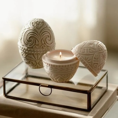 Velas esculpidas em cerâmica branca com padrões, sobre caixa de vidro e livro