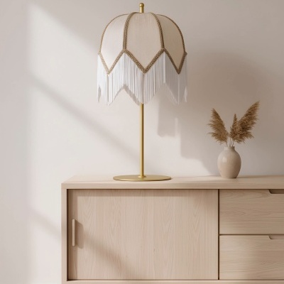 Candeeiro de mesa com cúpula branca e franjas sobre móvel de madeira clara com vaso decorativo