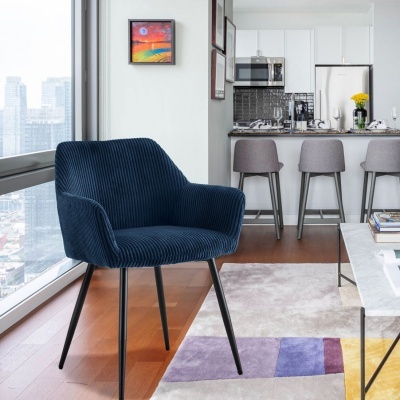 Cadeira azul escuro com pernas pretas perto de janela com vista para cidade, tapete colorido e cozinha branca com banquetas