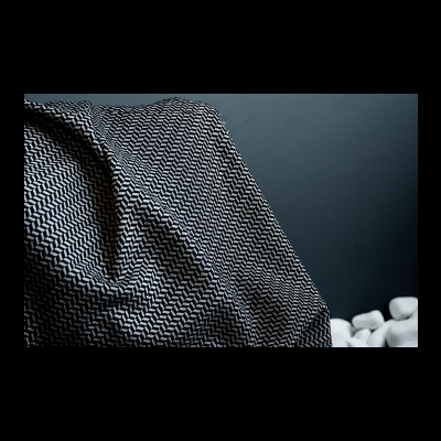 Tecido cinzento com padrão geométrico preto e branco sobre superfície com pedras brancas ao fundo