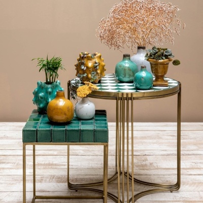 Mesas laterais com tampos de azulejos verdes e vasos cerâmicos decorativos com plantas e flores secas.
