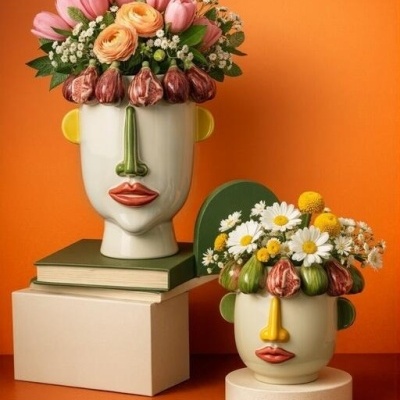 Vasos de cerâmica em forma de rosto com flores coloridas, fundo laranja.