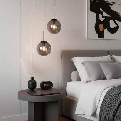 Mesa de cabeceira com vaso e relógio digital ao lado de cama cinzenta com lençóis brancos e cinzentos e luminárias pendentes de vidro fumado