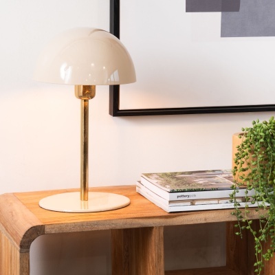 Candeeiro de mesa bege com haste dourada em móvel de madeira com livros e planta verde