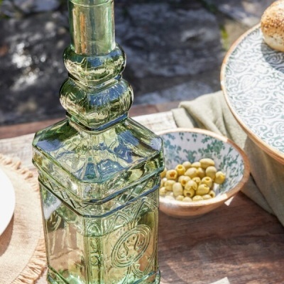 Garrafa de vidro verde translúcido com tampa de cortiça numa mesa de madeira com tigela de azeitonas