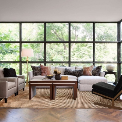 Sala de estar moderna com sofá branco, poltronas cinza, cadeira preta, mesa de centro de madeira, tapete bege e grande parede de janelas