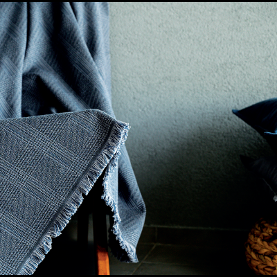 Cobertura cinzenta com padrão, almofadas cinza e azul, base de madeira entrelaçada, parede cinzenta