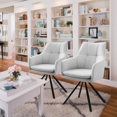 Duas cadeiras de tecido cinzento claro com pernas pretas em sala com estantes brancas cheias de livros e objetos.