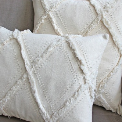 Almofadas bege claro com padrão em relevo e franjas sobre sofá cinzento