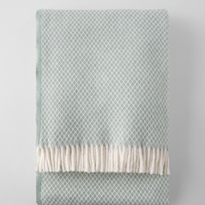 Manta verde-água com padrão branco e franjas brancas dobrada sobre fundo branco