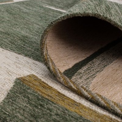 Tapete com padrão geométrico em verde, cinza e amarelo, mostrado em dobra que revela o verso com riscas finas.