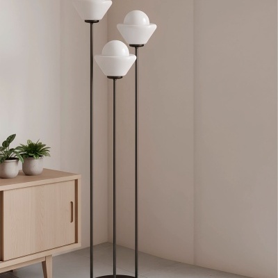 Candeeiro de pé com três abajures brancos e base e hastes negras junto a móvel de madeira e plantas.