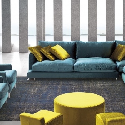 Sala de estar com sofá azul turquesa, poltronas, almofadas amarelas, mesa redonda amarela e candeeiros de chão azuis