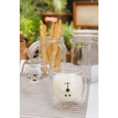 Dois copos de vidro decorados com desenhos de urso, jarros de vidro e plantas ao fundo