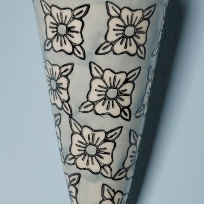 Vaso cerâmico branco com flores pretas e duas linhas pretas na borda contra parede azul