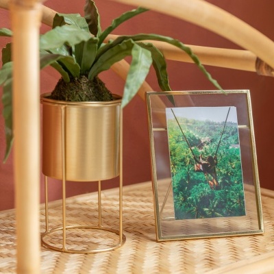 Vaso dourado com planta e porta-retrato dourado sobre mesa de rattan
