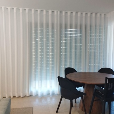 Mesa redonda de madeira com cadeiras pretas e cortinas brancas transparentes numa sala clara