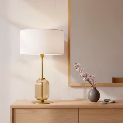 Lâmpada de mesa dourada com cúpula branca e vaso com flores num móvel de madeira clara
