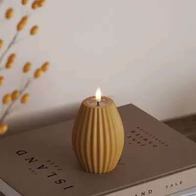 Vela amarela com textura ondulada acesa sobre livro castanho em ambiente interior