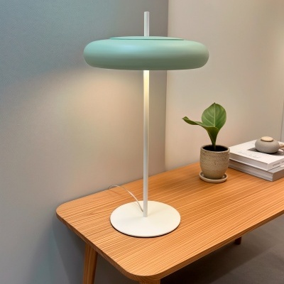 Lâmpada de mesa branca com cúpula verde clara sobre mesa de madeira com vaso de planta e livros