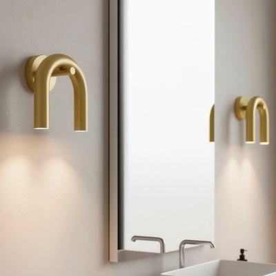 Luminária dourada em metal em forma de U invertido numa parede ao lado de espelho e pia branca com torneira