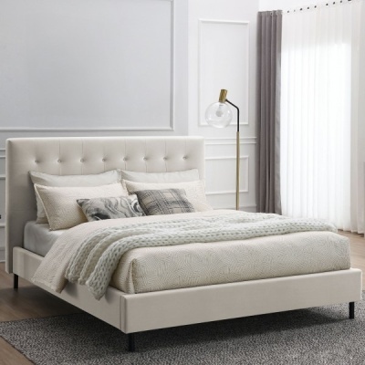 Cama branca estofada com roupa de cama creme, manta grossa, candeeiro dourado com globo de vidro, cortinas cinza e tapete cinza