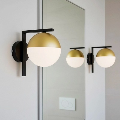 Aplique de parede preto com cúpula esférica dourada e branca junto a um espelho fino cinza