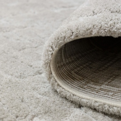 Tapete felpudo creme com textura macia e verso em padrão xadrez.