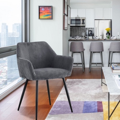 Cadeira cinzenta riscada com pernas pretas numa sala com janela grande e cozinha ao fundo