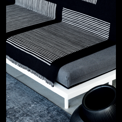 Sofá cinza com manta preta de riscas brancas e objeto decorativo preto.