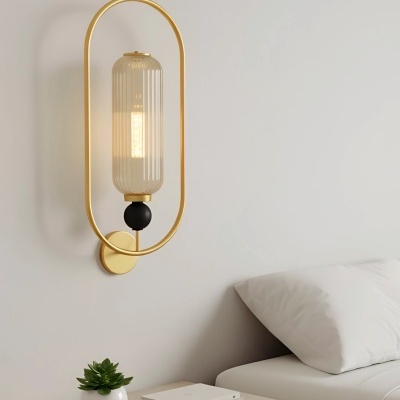 Candeeiro de parede dourado com vidro transparente sobre mesa de cabeceira com planta e livros ao lado de cama branca