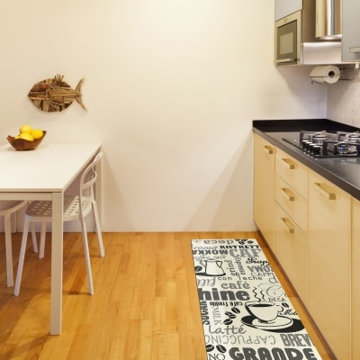 Cozinha moderna com armários creme, tampo preto, tapete de café preto e branco, mesa branca e cadeiras brancas.