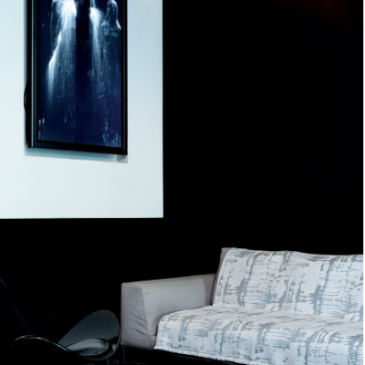 Sofá cinzento, cadeira preta moderna e quadro artístico com três figuras humanas em parede branca e preta