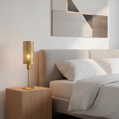 Mesa de cabeceira em madeira clara com lâmpada dourada perfurada ao lado de uma cama com cabeceira cinzenta e roupa de cama branca