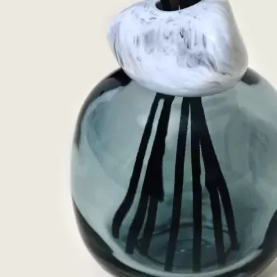 Frasco redondo de vidro cinza fumado com tampa de mármore branco e preto e varetas de aromatizador preto