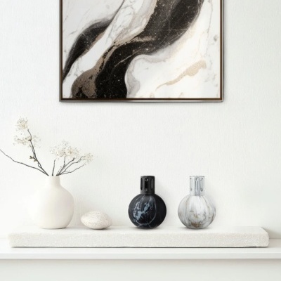 Três vasos decorativos com padrões de mármore sobre prateleira branca com base clara, quadro abstrato tons preto, branco e bege por trás.