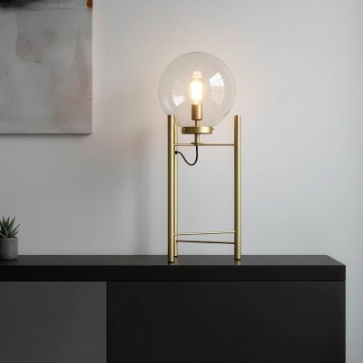 Lâmpada de mesa dourada com abajur em vidro transparente em forma de globo sobre móvel preto