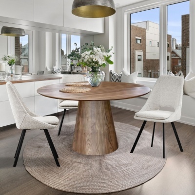 Mesa de madeira redonda com cadeiras brancas estofadas e tapete redondo em sala iluminada