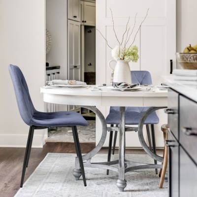 Mesa de jantar branca redonda com cadeiras azuis e vaso com flores em ambiente claro