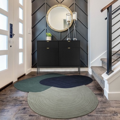 Tapete moderno com três áreas circulares em cinzento claro, azul escuro e verde em chão de madeira, ao lado de cómoda preta com espelho redondo
