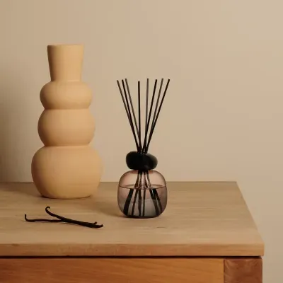 Vaso de cerâmica beige arredondado e aromatizador de ambiente com frasco de vidro e varetas pretas.