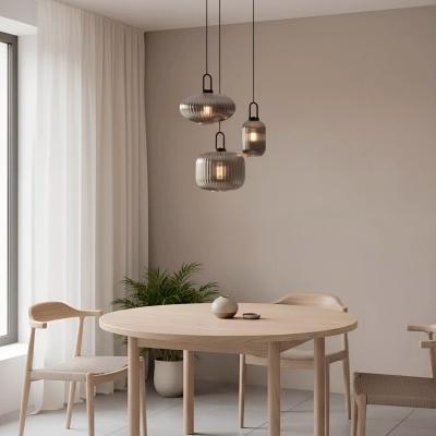 Mesa de jantar redonda em madeira clara com três cadeiras de madeira e assento tecido bege, três candeeiros suspensos de vidro cinza, vaso cerâmico e planta