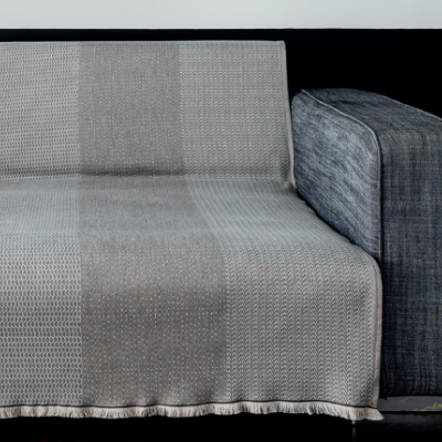 Sofá cinzento escuro com manta de faixas neutras em bege e cinza sobre assento e encosto